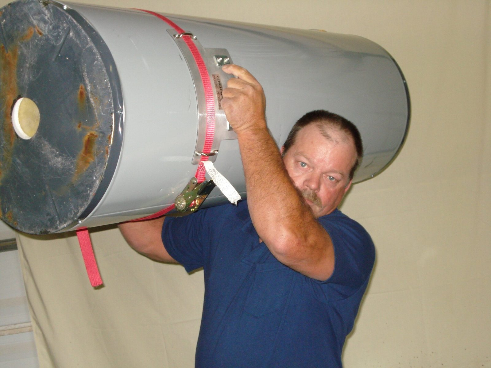 A plumber carrying a water heater on his shoulder by its CINCH-N-LIFT handle