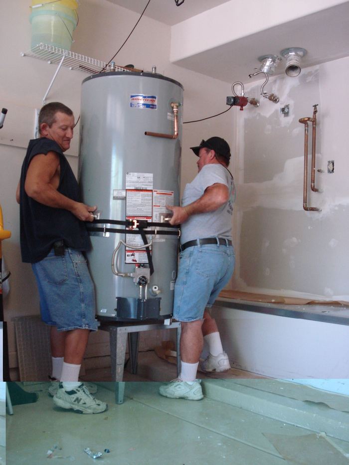 Two men setting a 75-gallon gas water heater onto its stand